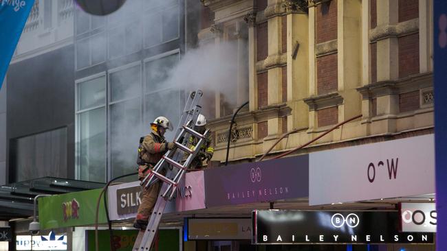 Members of the SA Metropolitan Fire Service climb through a window as toxic smoke billows from a heritage building on Rundle Mall. Picture: AAP/Emma Brasier