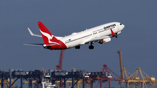 This picture taken on December 6, 2023 shows a Qantas Airways Boeing 737-800 passenger aircraft taking off at Sydney’s Kingsford Smith international airport in front of a container ship berthed at the Port Botany container terminal. (Photo by DAVID GRAY / AFP)