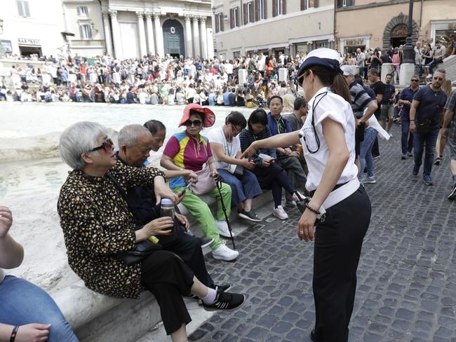 A city police officer talks to tourists gathered in front of Trevi fountain, in Rome, Friday, June 7, 2019. Tired of ad hoc bans on ill behavior by tourists, Rome has converted its temporary crackdowns into one big law. The city announced Friday that the city council had a day earlier approved the all-encompassing law. Most bans, like frolicking in monumental fountains or eating lunch on monuments, had been in effect for some time, but needed to be periodically renewed. (AP Photo/Gregorio Borgia)