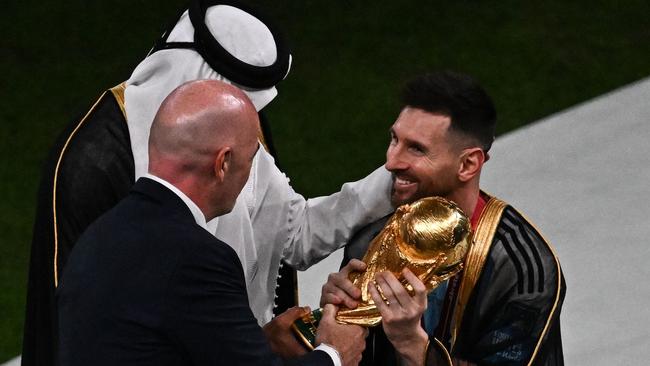 Argentina's forward #10 Lionel Messi (R) receives the World Cup Trophy from Qatar's Emir Sheikh Tamim bin Hamad al-Thani (L) and FIFA President Gianni Infantino.