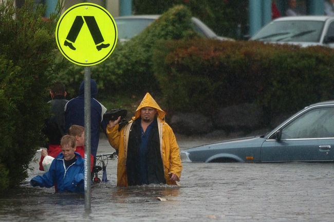 Gold Coast, June 30, 2005. An unidentified man with two children cross a flooded intersection in front of a submerged car at Varsity Lakes on Queensland’s Gold Coast today. Widespread flooding has hit the popular tourist area, known for its sunshine and sandy beaches, with reports of rainfall reaching 80mm per hour in some regions. (AAP Image/Tony Phillips)