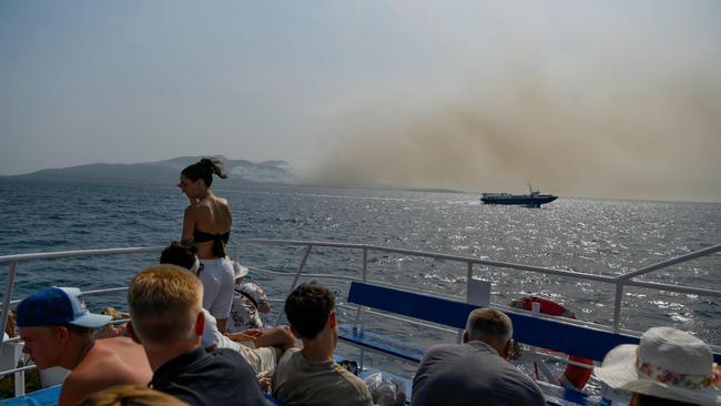 Tourists ride on a ferry to Corfu island as the smoke billows from the fire over the island. Picture: AFP