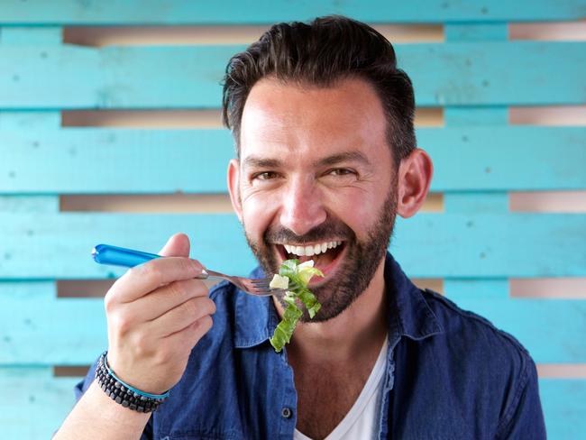Close up portrait of cheerful man eating salad from bowl