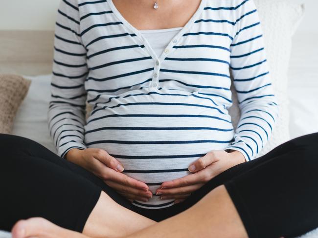 Pregnant woman in striped t-shirt sitting on the bed touching her belly and relaxing. Close up