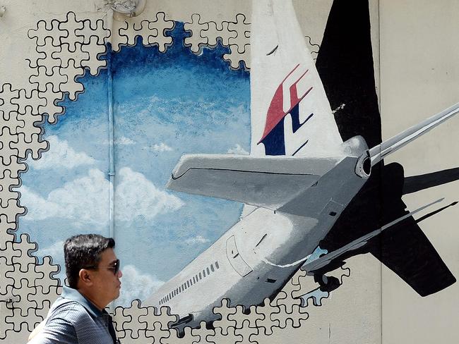 (FILES) This file photo taken on March 8, 2016 shows a Malaysian man walking in front of a mural of missing Malaysia Airlines MH370 plane in a back-alley in Shah Alam. The disappearance of the Boeing 777 carrying 239 passengers and crew almost four years ago is one of aviation's greatest mysteries, with an Australian-led hunt across a 120,000 square-kilometre (46,000 square-mile) zone failing to reveal the crash site.  / AFP PHOTO / Manan VATSYAYANA / TO GO WITH Australia-Malaysia-China-aviation-MH370,FOCUS by Glenda Kwek