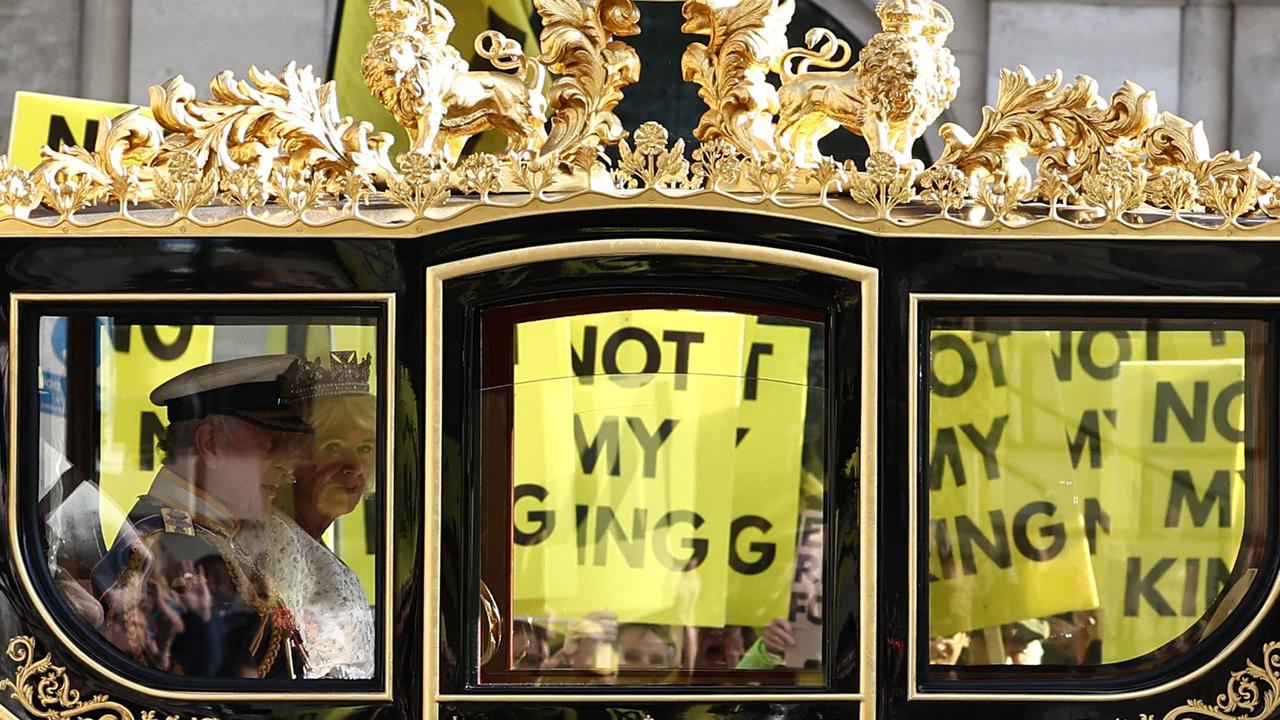 King Charles III and Queen Camilla travel in the Diamond Jubilee State Coach past protesters holding 