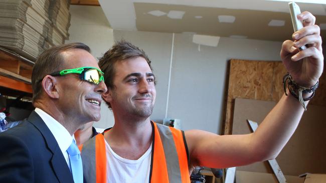 Prime Minister Tony Abbott gets a selfie with worker Emerson Smith during his visit the Timbermate factory in the Melbourne suburb of Mitcham. Friday, Feb. 6, 2015. The Prime Minister was visiting to talk about how a carbon tax would effect small business. (AAP Image/David Crosling) NO ARCHIVING