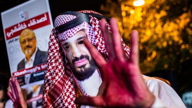 A protestor wears a mask of depicting Saudi Crown Prince Mohammad Bin Salman with red painted hands next to people holding posters of Saudi journalist Jamal Khashoggi  during the demonstration outside the Saudi Arabia consulate in Istanbul, on October 25, 2018. - Jamal Khashoggi, a Washington Post contributor, was killed on October 2, 2018 after a visit to the Saudi consulate in Istanbul to obtain paperwork before marrying his Turkish fiancee. (Photo by Yasin AKGUL / AFP)