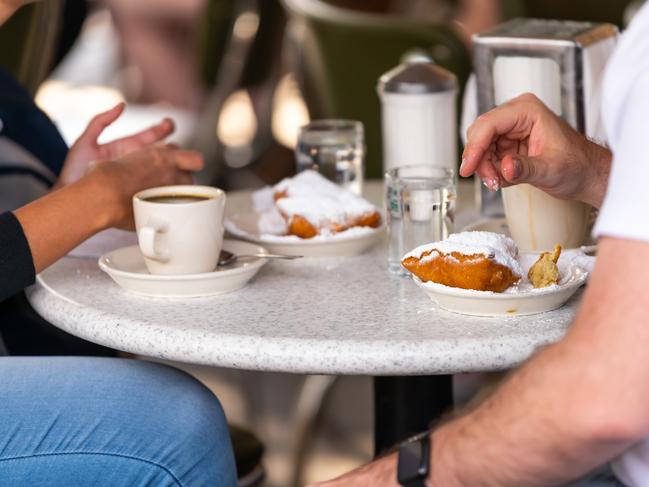 ESCAPE:  Closeup of couple sitting outside at sidewalk cafe by table drinking chicory coffee and eating deep fried beignet donut powdered with sugar Picture: Istock