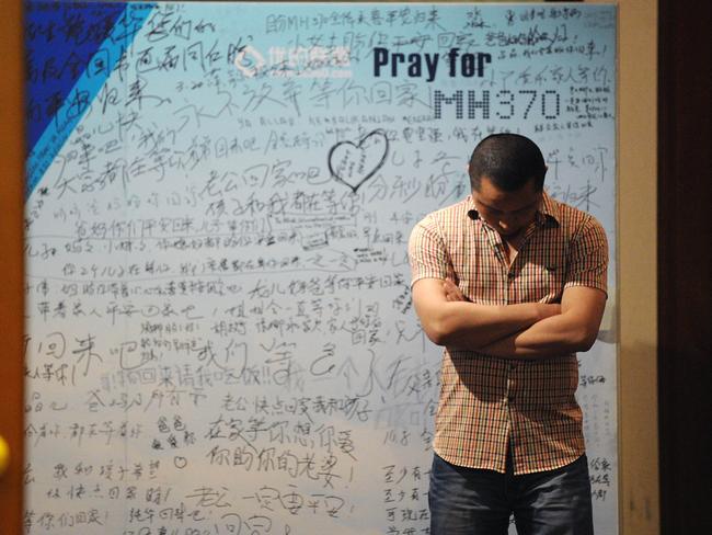 What’s the cost of a life? A man stands in front of a billboard in support of missing flight MH370. AFP Photo/Wang Zhao