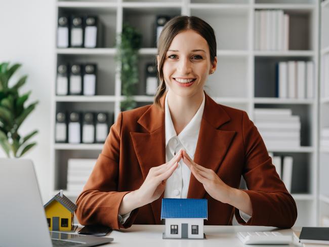 Female real estate agent is use hands to protect red roof for the concept of real estate investment about house trading, purchase at desk in office;  woman property investing generic