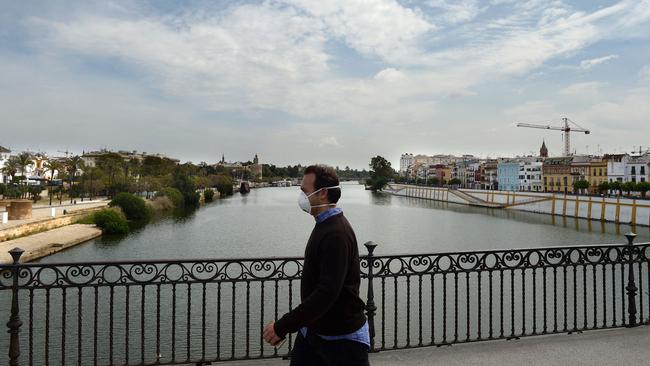 A man wearing a face mask crosses the Triana bridge over the Guadalquivir river in Seville, Spain. Picture: AFP