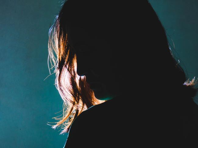 silhouette of depress woman standing in the dark with light shine behind