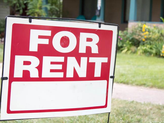 A blank red and white for rent sign is posted in the front yard of a home. The home has a porch and is a rental property.