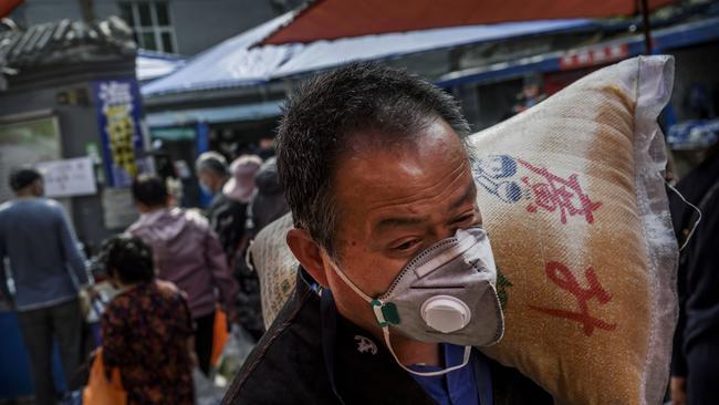 A Chinese man wears a protective mask as he carries a bag of grain at a local outdoor market in Beijing, China. Photo: Kevin Frayer/Getty Images