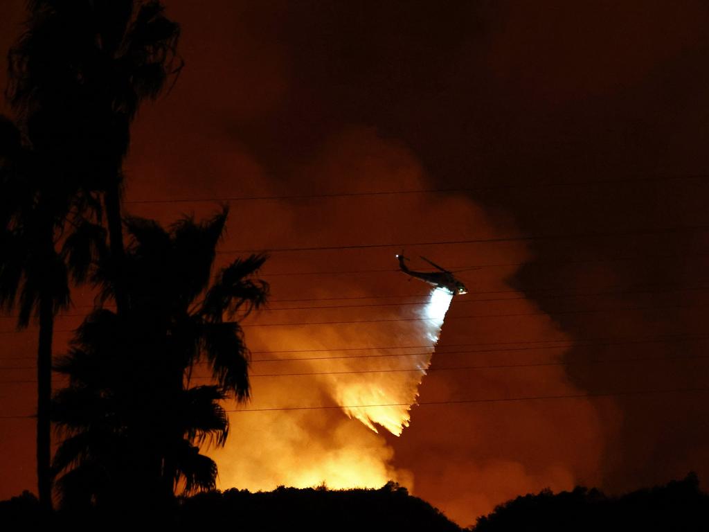 A firefighting helicopter drops water as the Palisades fire burns toward the Mandeville Canyon neighbourhood. Picture: AFP