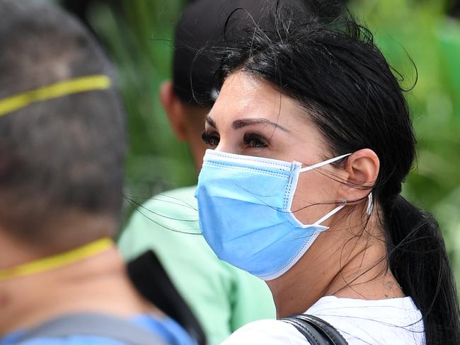 People are seen wearing face masks in a long queue outside the Centrelink office in Southport on the Gold Coast, Monday, March 23, 2020. Centrelink offices around Australia have been inundated with people attempting to register for the Jobseeker allowance in the wake of business closures due to the COVID-19 pandemic.  (AAP Image/Dan Peled) NO ARCHIVING