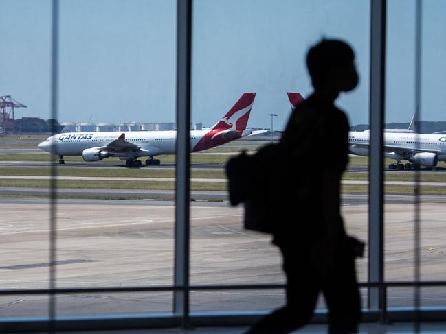 SYDNEY, AUSTRALIA - NewsWire Photos December 9, 2020: Qantas aircraft seen on the runway as a passenger passes through the terminal in the foreground at Sydney International Airport. Picture: NCA NewsWire / James Gourley