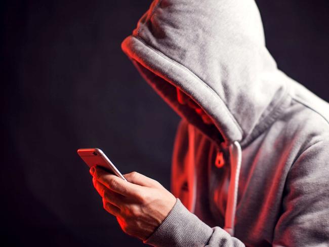 Man wearing hoody sweater with mobile phone in hands. Crime and hacking concept; scam generic.