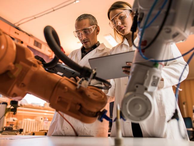 Low angle view of two engineers working on robotic arm in laboratory. Woman is using digital tablet.