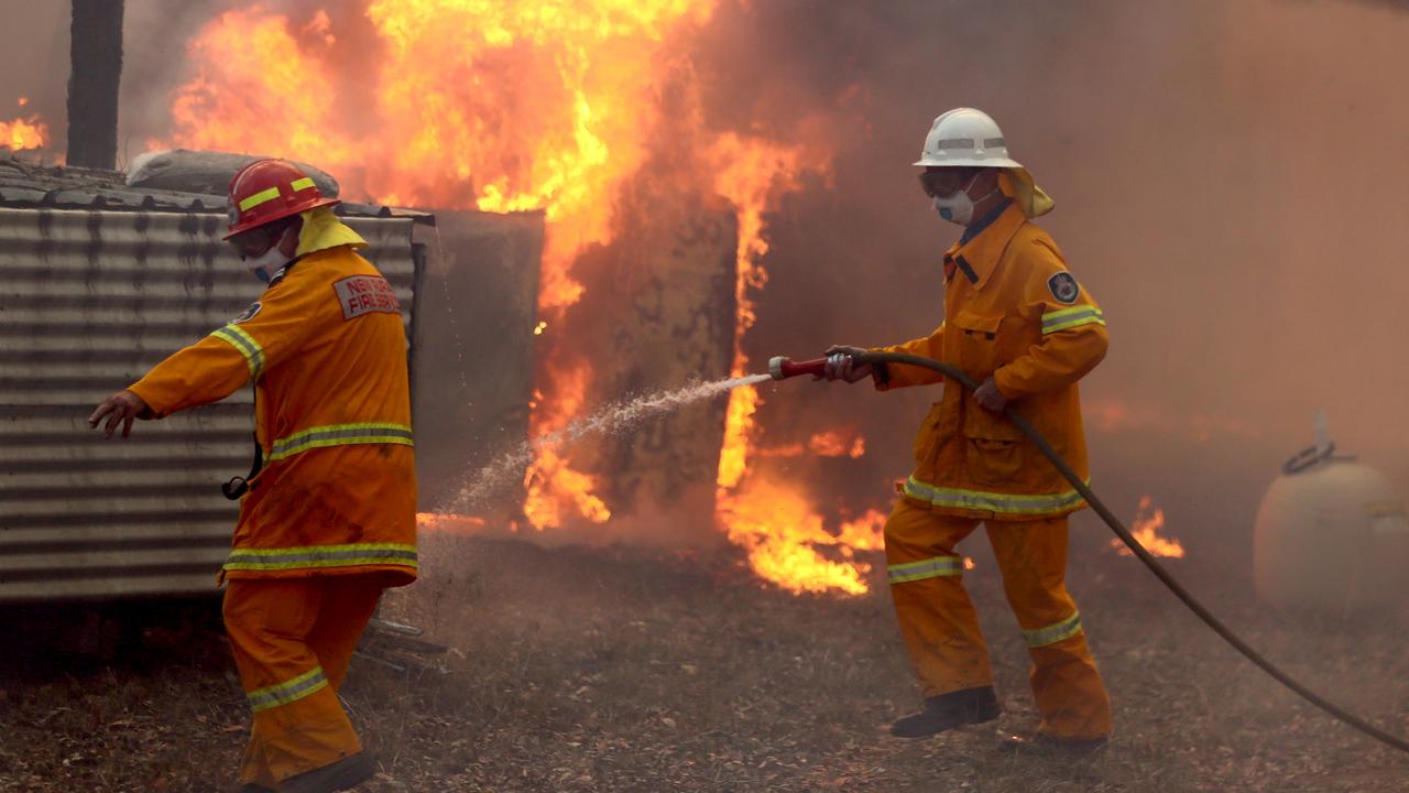 Firefighters hold back a fire threatening a house on The Buckets Way at Tinonee near Taree on the NSW mid north coast. Picture Nathan Edwards.