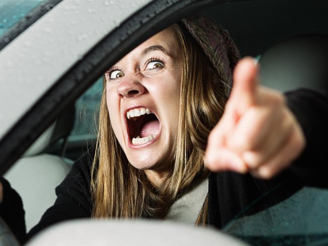 A young woman yells and points at something or someone in a fit of road rage, seen through her car window.