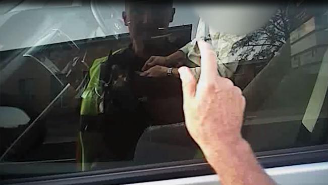 A police officer taps on the window of a car to alert a driver engrossed in his phone while stopped at traffic lights.