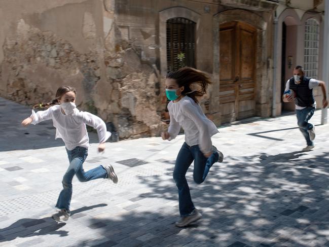 TOPSHOT - Joan, 45, chases his daughters Ines, 11, and Mar, 9, as they play in the street on April 26, 2020, in Barcelona, during a national lockdown to prevent the spread of the COVID-19 disease. - After six weeks stuck at home, Spain's children were being allowed out today to run, play or go for a walk as the government eased one of the world's toughest coronavirus lockdowns. Spain is one of the hardest hit countries, with a death toll running a more than 23,000 to put it behind only the United States and Italy despite stringent restrictions imposed from March 14, including keeping all children indoors. Today, with their scooters, tricycles or in prams, the children accompanied by their parents came out onto largely deserted streets. (Photo by Josep LAGO / AFP)