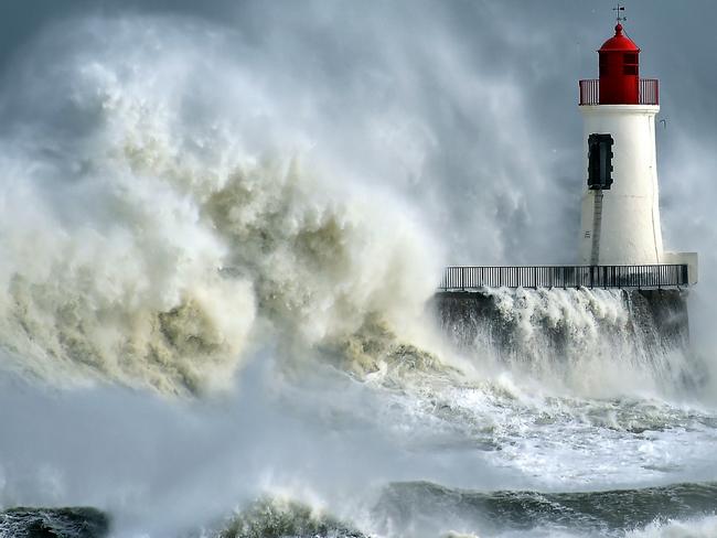 TOPSHOT - A waves breaks against a pier and a lighthouse in Les Sables-d'Olonne, western France, on February 9, 2016. High winds buffeted northwestern Europe on February 8, leaving one woman in France in a coma after she was hit by an advertising hoarding. Electricity was cut to 5,000 homes in northern France. / AFP / LOIC VENANCE