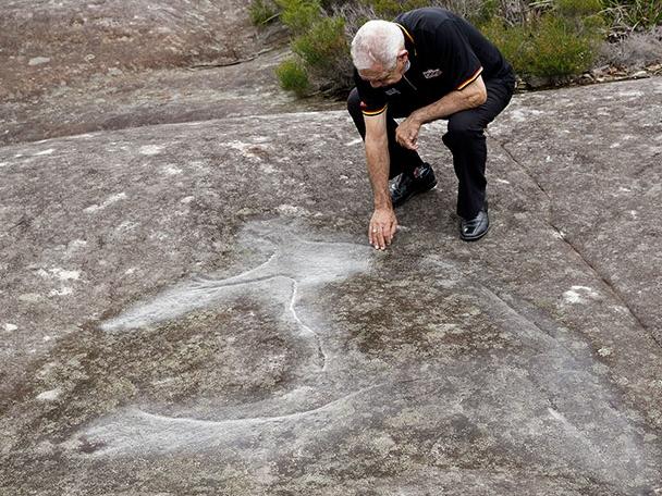 Gadigal Elder Uncle Allen Madden with a rock carving within the Lizard Rock land holding. Picture: Metropolitan Local Aboriginal Land Council