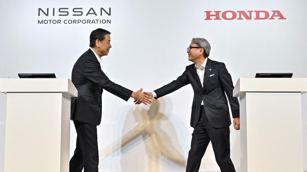 Makoto Uchida (L), president and CEO of Japanese automaker Nissan, and Toshihiro Mibe (R), director, president and representative executive officer of automaker Honda, shaking hands at the start of in a press conference in Tokyo. (Photo by Richard A. Brooks / AFP)