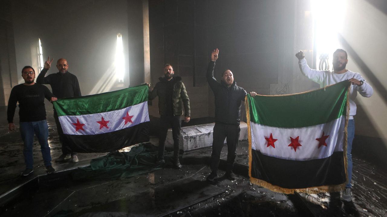 Rebel fighters stand with the flag of the revolution on the burnt gravesite of Syria's late president Hafez al-Assad on December 11, 2024. Picture: Aaref Watad/AFP