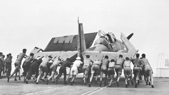 All hands on deck as HMS Pioneer crew push a WWII Grumman Avenger torpedo fighter on an aircraft carrier off Sydney in January 1946.