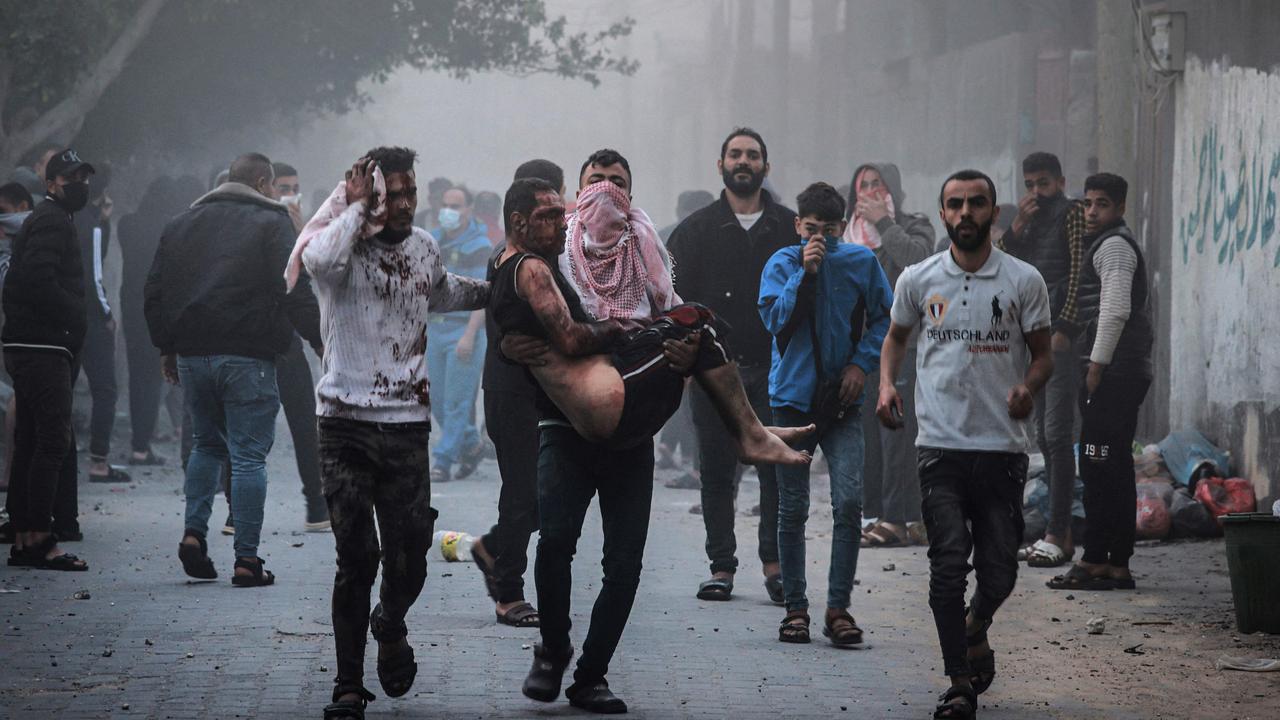 A Palestinian man carries an injured man as people flee following an Israeli strike in Rafah in the southern Gaza Strip on November 23, 2023, amid ongoing battles between Israel and the Palestinian militant group Hamas. (Photo by MOHAMMED ABED / AFP)