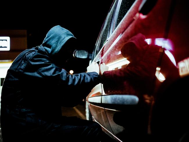 Car thief  in action late at night, wearing a black mask on his head