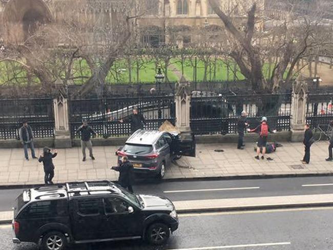 People stand near a crashed car and an injured person lying on the ground, right, on Bridge Street near the Houses of Parliament in London. Picture: AP