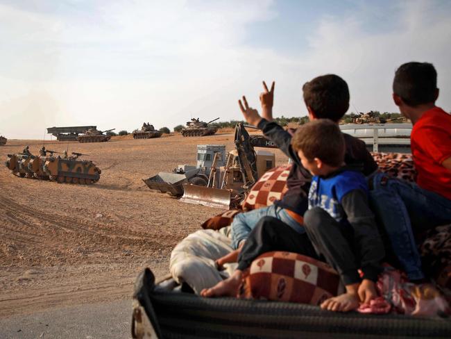 Syrian Arab civilians flash the victory sign as Turkish armoured personnel carriers and US-made M60 tanks gather in the village of Qirata. Picture: AFP