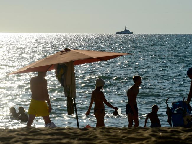 People relaxing on a beach of the Black Sea in Sevastopol, the largest city on the Crimean Peninsula and its most important port and naval base, with a Russian warship seen in the background in July 2022. Picture: Olga Maltseva/AFP