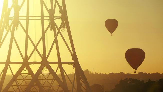 Hot air balloons drift over Melbourne's Arts Centre at sunrise.