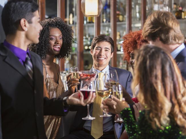 A multiethnic group of young adults drinking together at a bar. The men are in business suits and the women are wearing cocktail dresses.