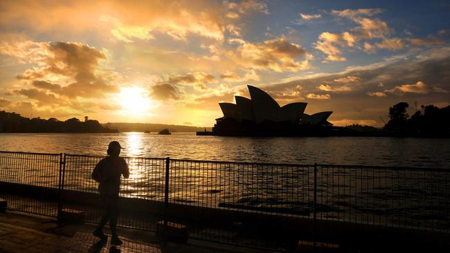 The sun rises next to the Sydney Opera House as a jogger trains at the overseas passenger terminal at Circular Quay. Picture: Damian Shaw