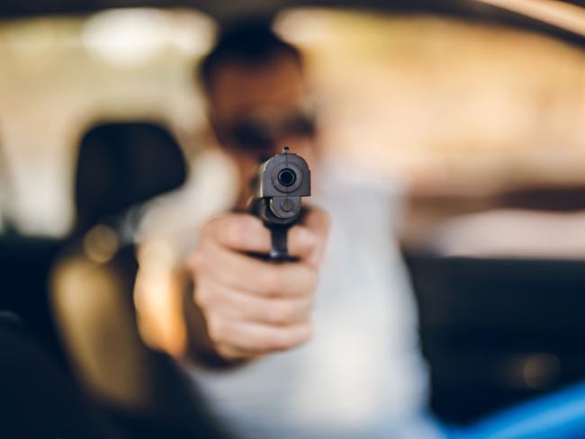 Man driving a car and holding a gun. Sunset.