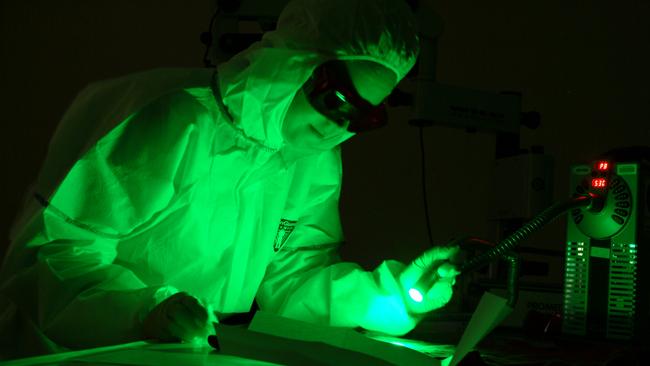 An AFP forensic officer working on a case using the latest Polilight technology. Picture AFP