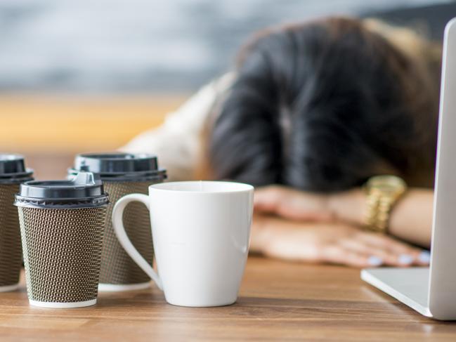 A female entrepreneur and businesswoman is working on her start up company in her office. She has fallen asleep at the office with her head on her desk. Empty coffee cups are on the table.