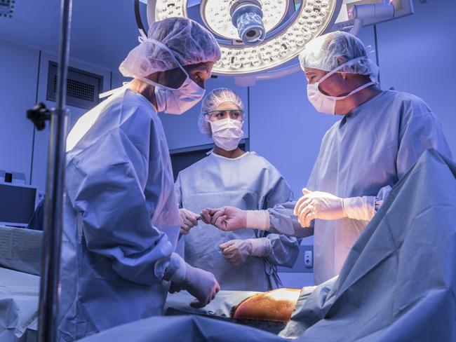 Doctors wearing surgical masks and gowns performing an operation on patient in hospital operating theater.