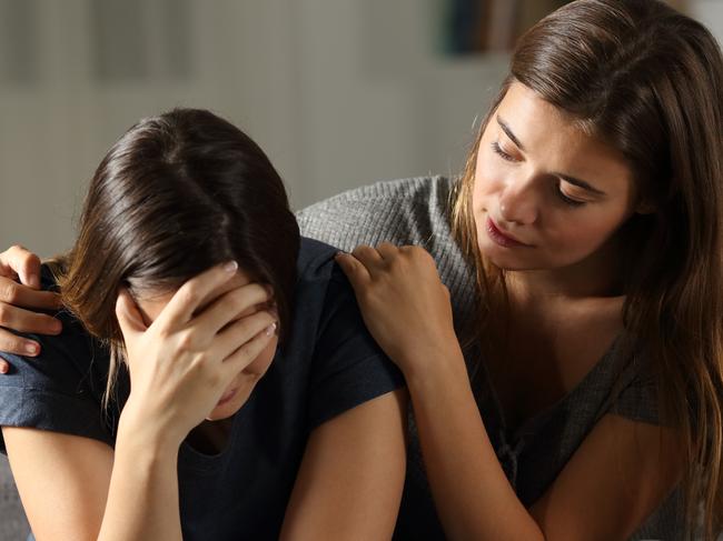 Teen comforting hes sad friend in the night sitting on a couch in the living room at home