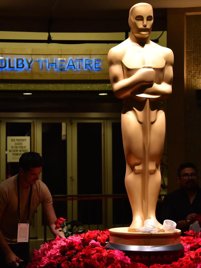 Workers arrange flowers next to an Oscar statue.