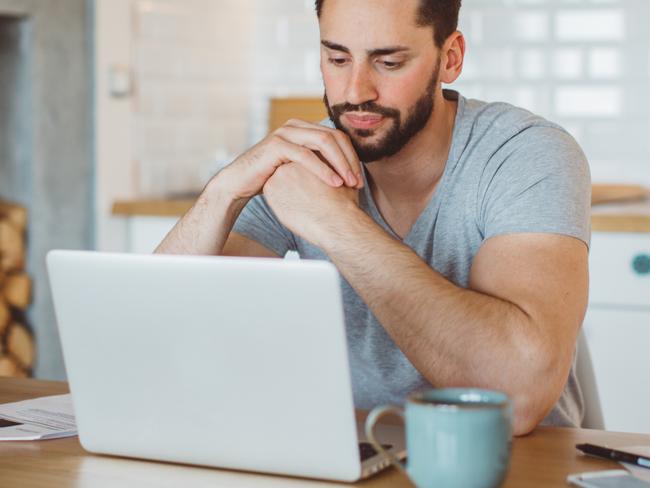 Young man worried about his finances at home. He is wearing pajamas and drinking first coffee of the day at the kitchen.