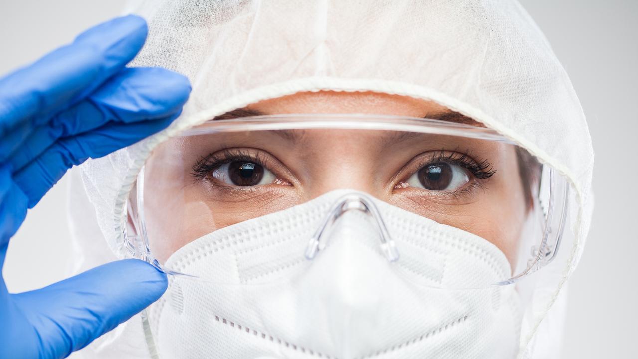 Female lab scientist,doctor or nurse,putting protective eyewear goggles,wearing blue gloves,N95,PPE clean suit,portrait of UK NHS front line medical staff handling COVID-19 pandemic crisis in hospital