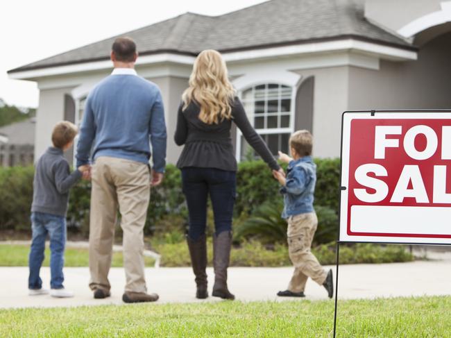 Family with two boys (4 and 6 years) standing in front of house with FOR SALE sign in front yard.  Focus on sign.